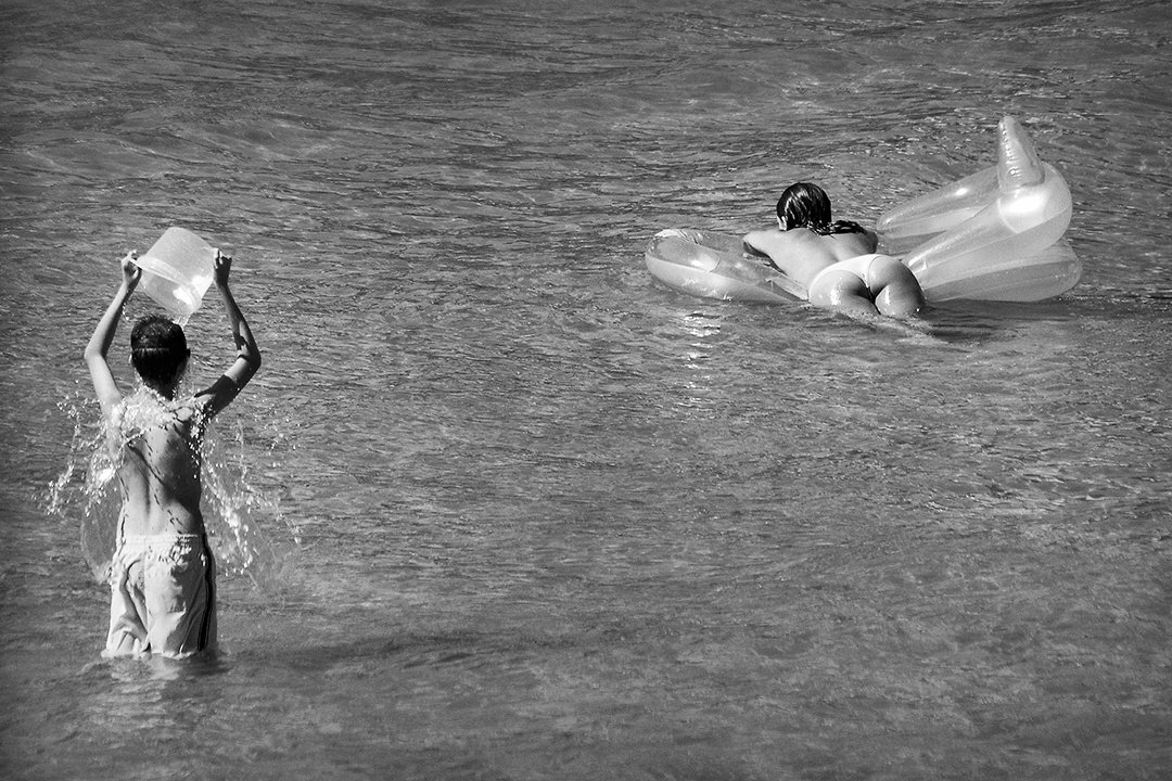 A person lifts a container in the water beside an inflatable mattress.